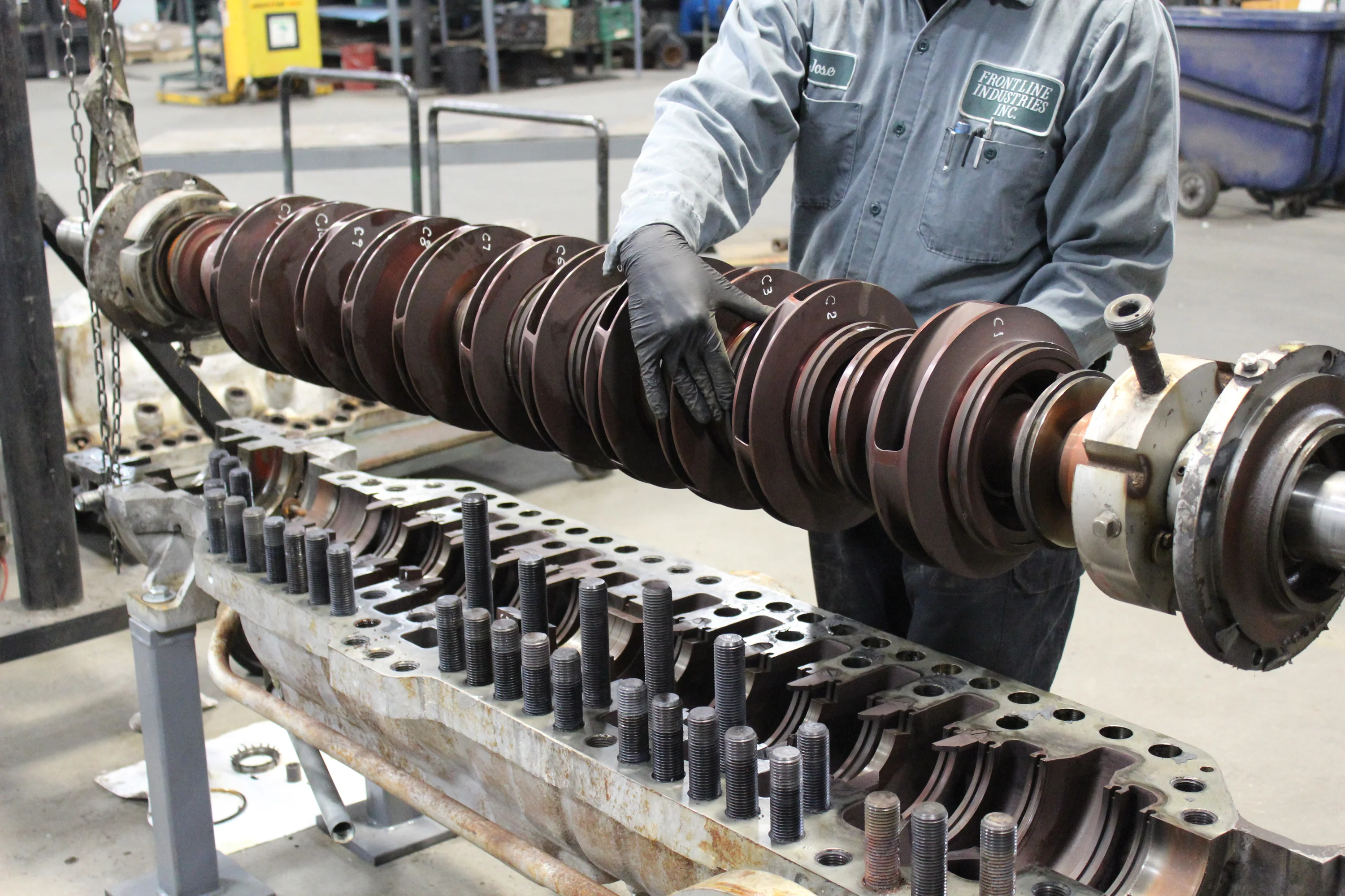 Frontline technician handling a pump rotor above an open casing in the shop